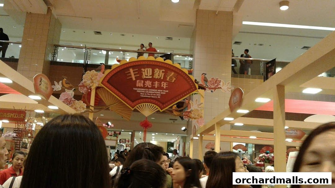 A festive Chinese New Year display with a large fan and floral decorations in a shopping mall.