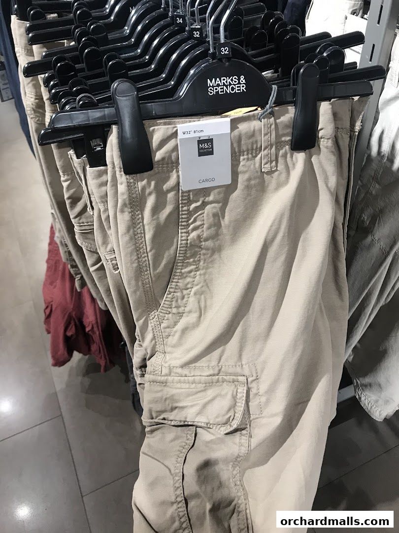 Close-up of beige cargo pants hanging on hangers with size tags.