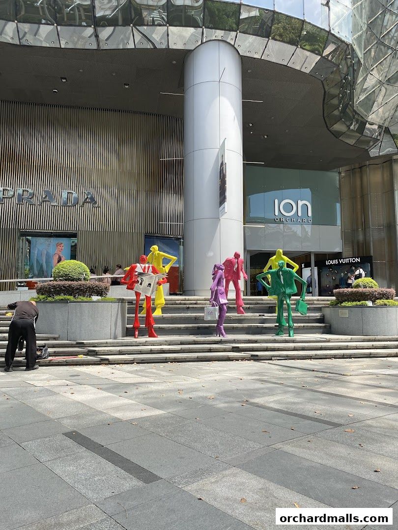 Colorful sculptures stand outside a modern shopping mall with Prada and Louis Vuitton stores.