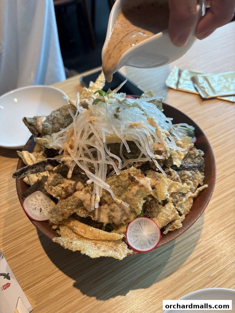A bowl of crispy unagi skin salad with radish and dressing being poured.