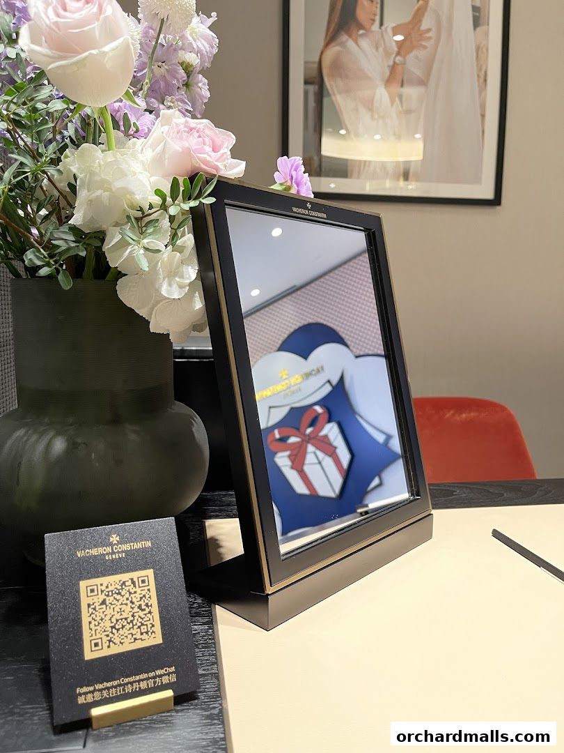 A Vacheron Constantin display with flowers, a QR code, and a framed reflection of a gift.