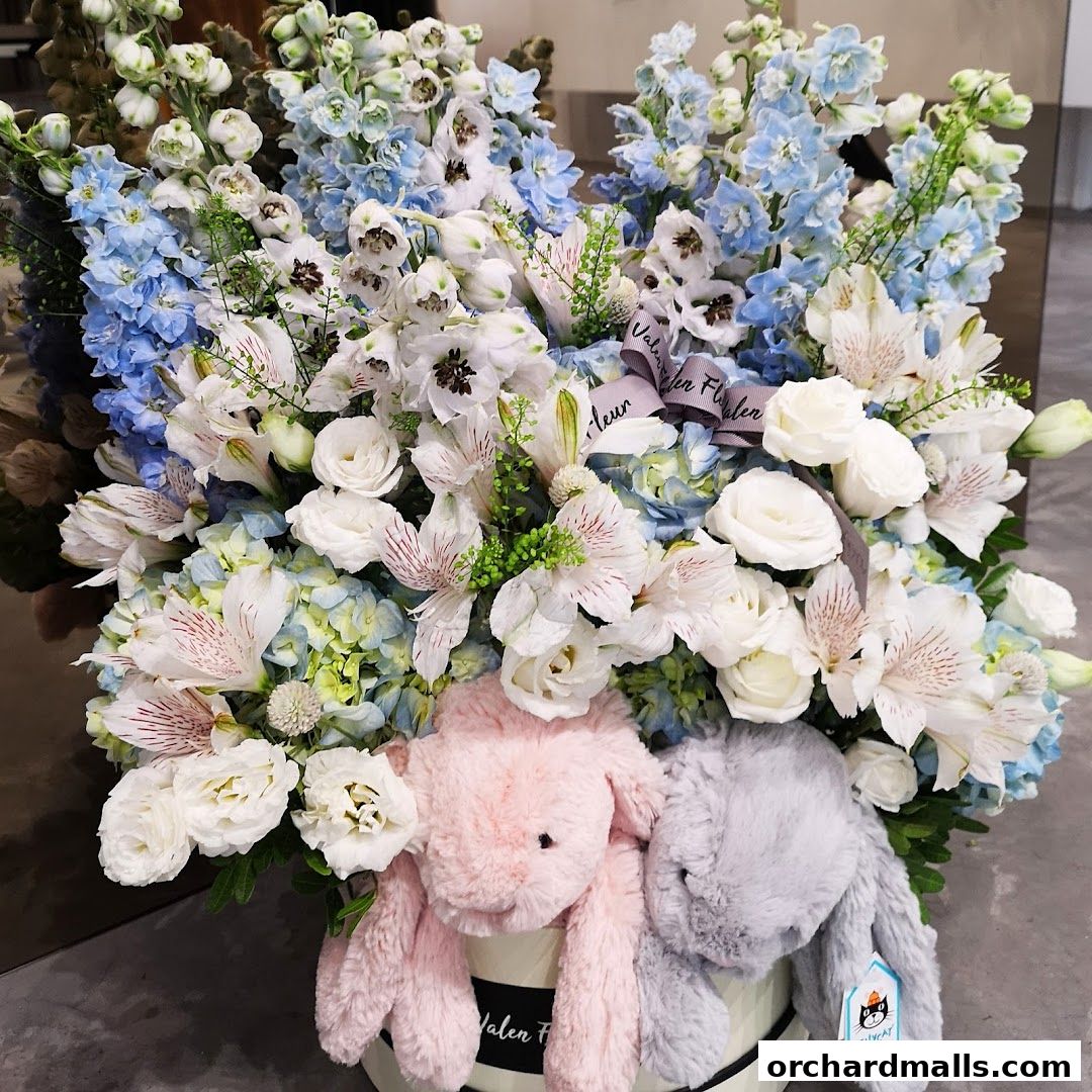 A beautiful floral arrangement with two plush bunnies in a round box.