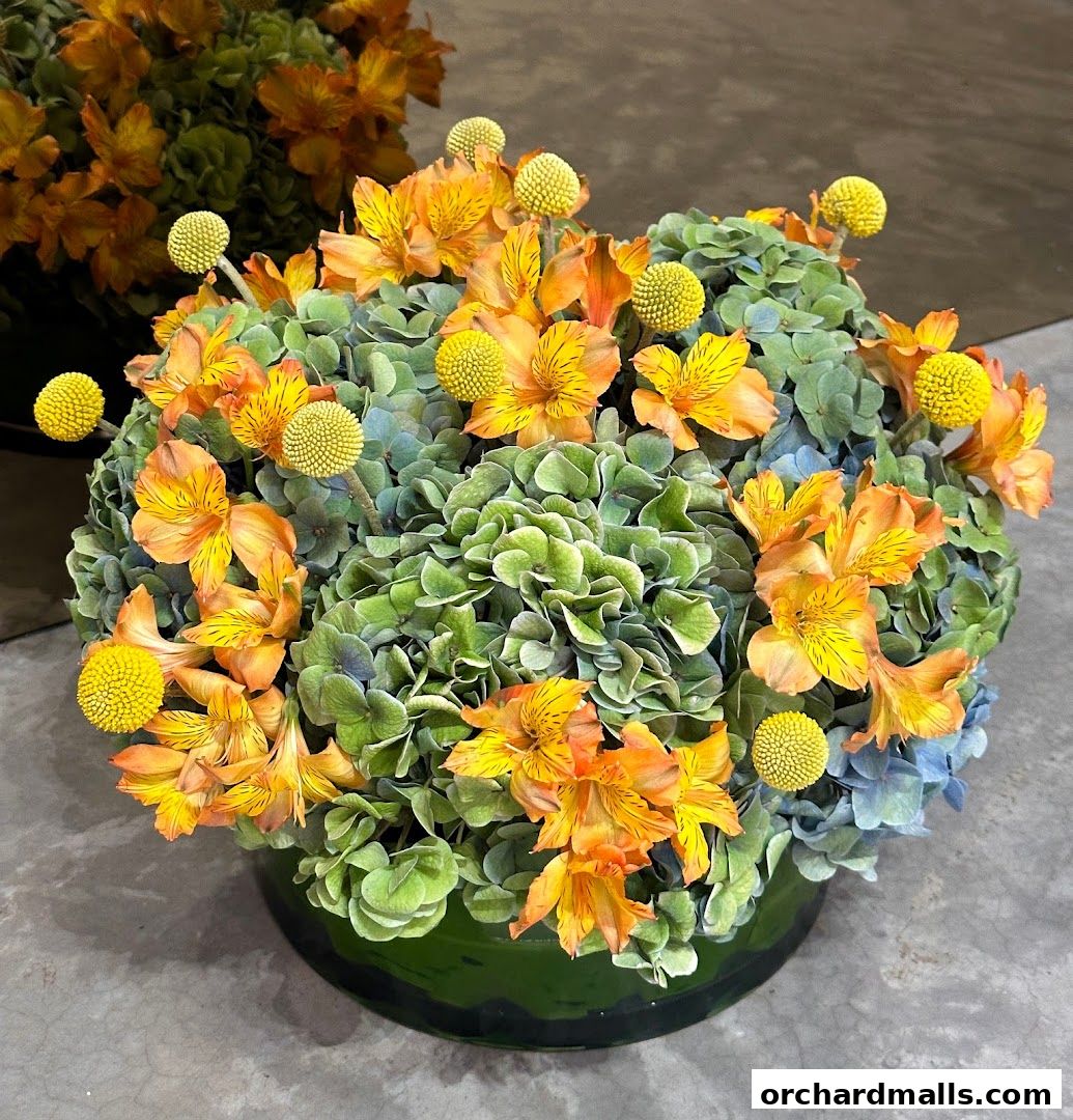 A vibrant floral arrangement featuring orange lilies, yellow craspedia, and green hydrangeas in a green vase.