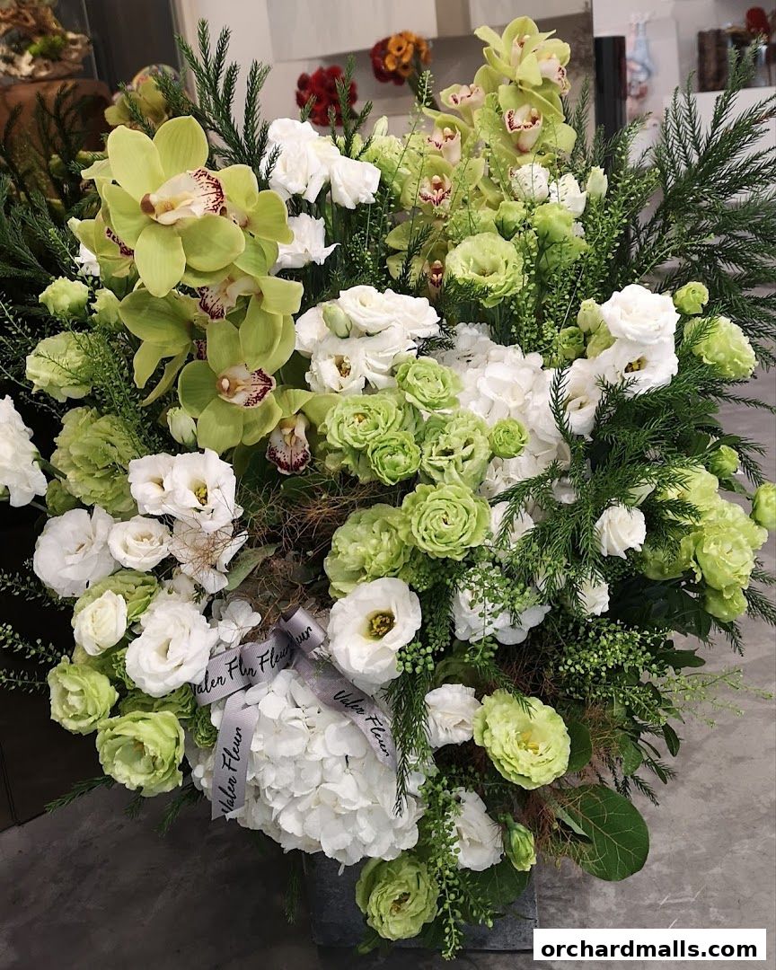 A large, lush floral arrangement featuring green orchids, white roses, and hydrangeas.