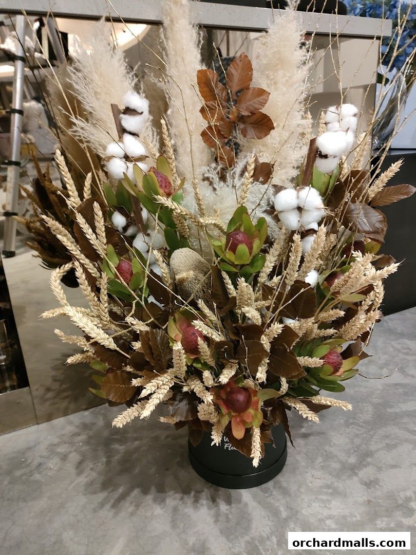 A dried floral arrangement with cotton, protea, and wheat in a black box.