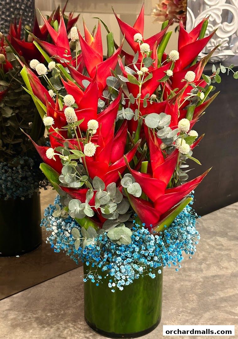 A vibrant floral arrangement featuring red heliconia flowers and blue baby's breath in a green vase.