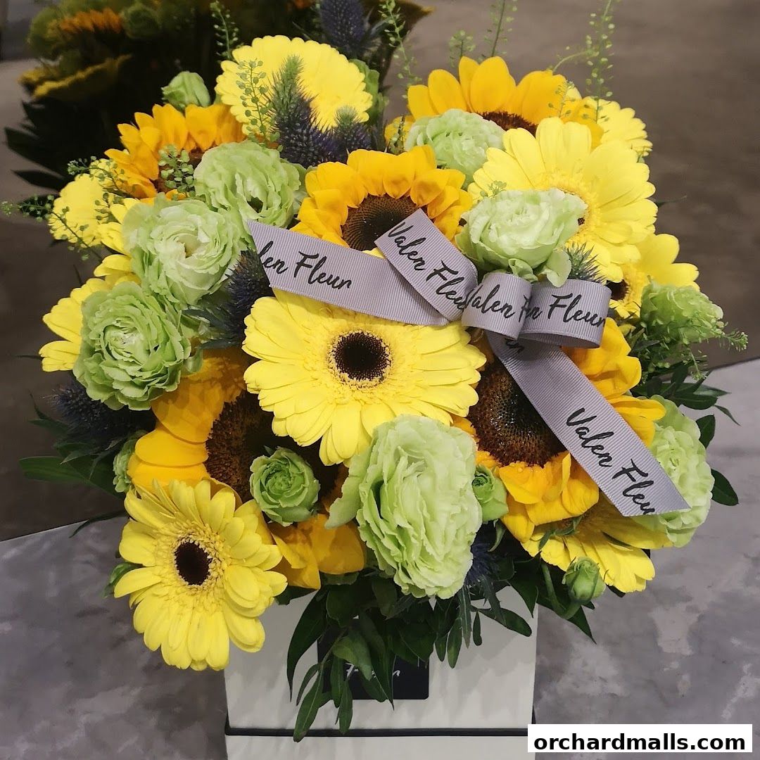A vibrant bouquet of sunflowers and green flowers with a branded ribbon.