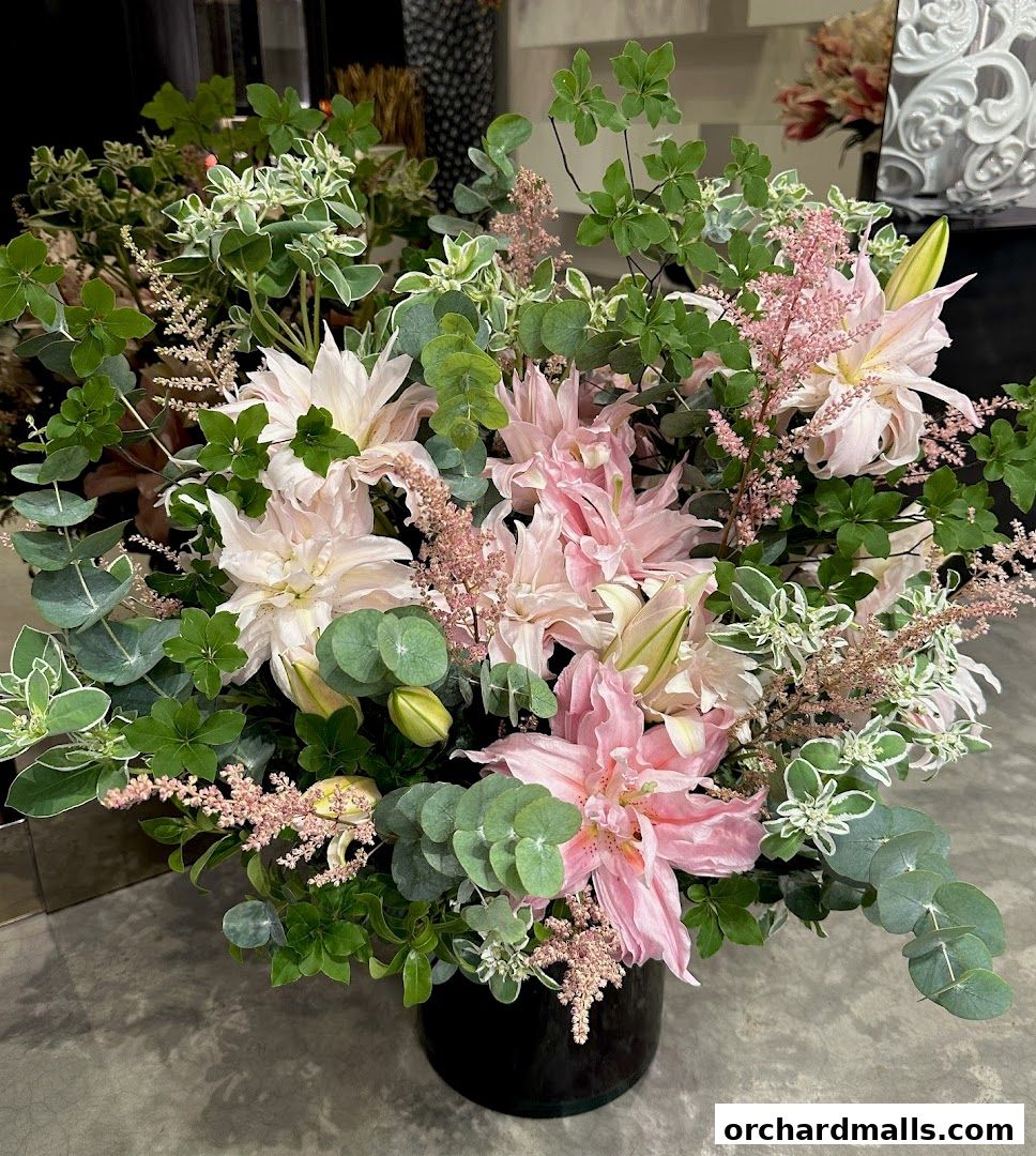 A beautiful arrangement of pink lilies, eucalyptus, and other greenery in a black vase.