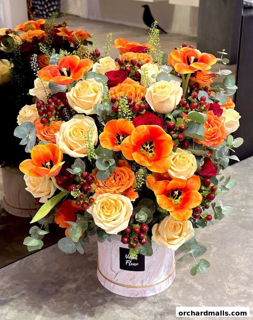 A vibrant floral arrangement in a marble-patterned box with roses, tulips, and berries.