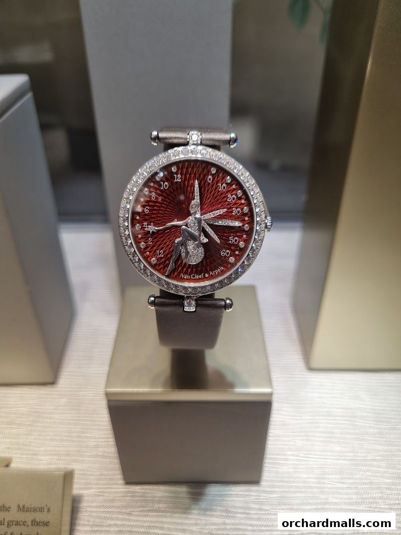 A close-up of a Van Cleef & Arpels watch with a red dial and diamond-encrusted bezel.
