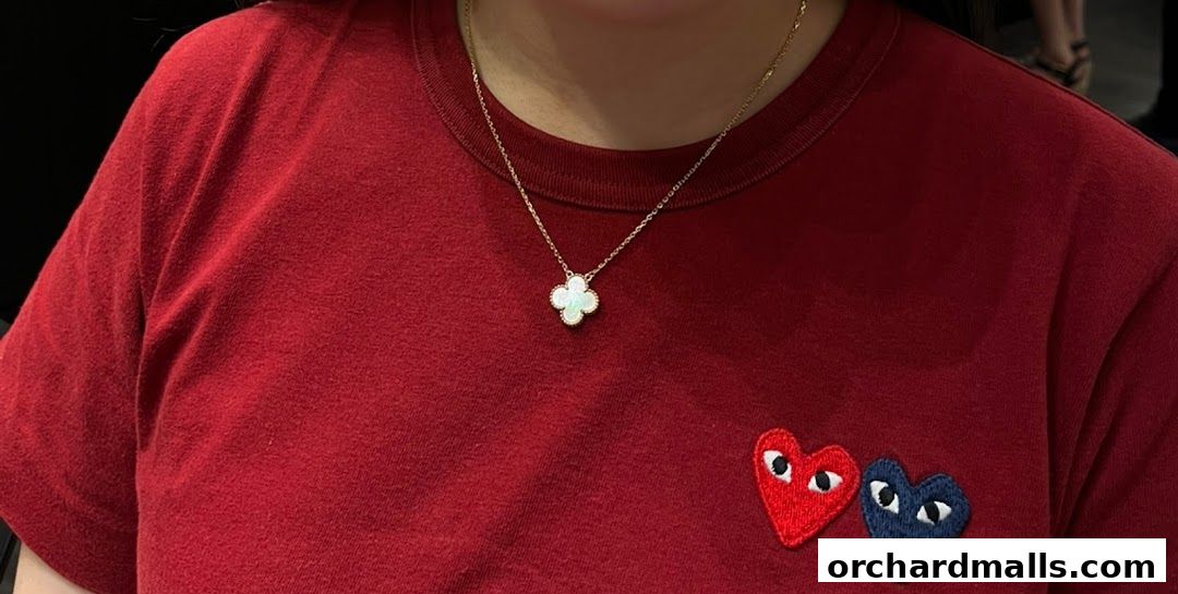 A person wearing a red t-shirt with a Van Cleef & Arpels necklace and heart patches.