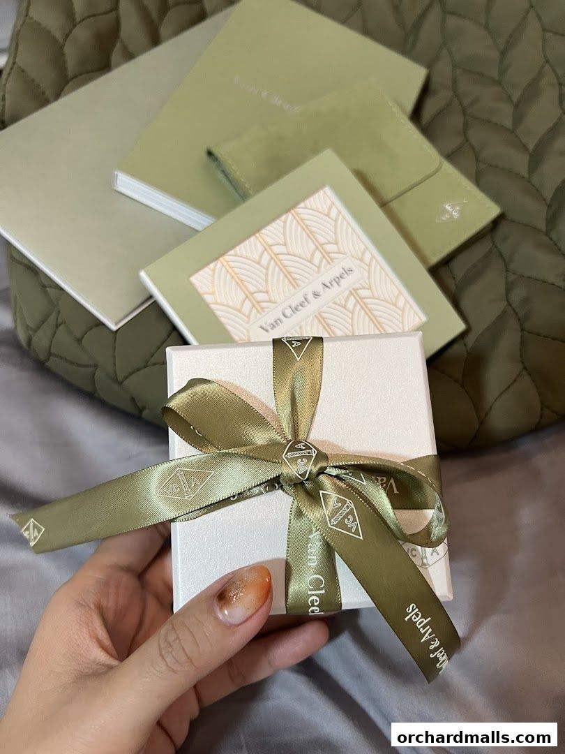 A hand holds a Van Cleef & Arpels gift box tied with a branded ribbon.