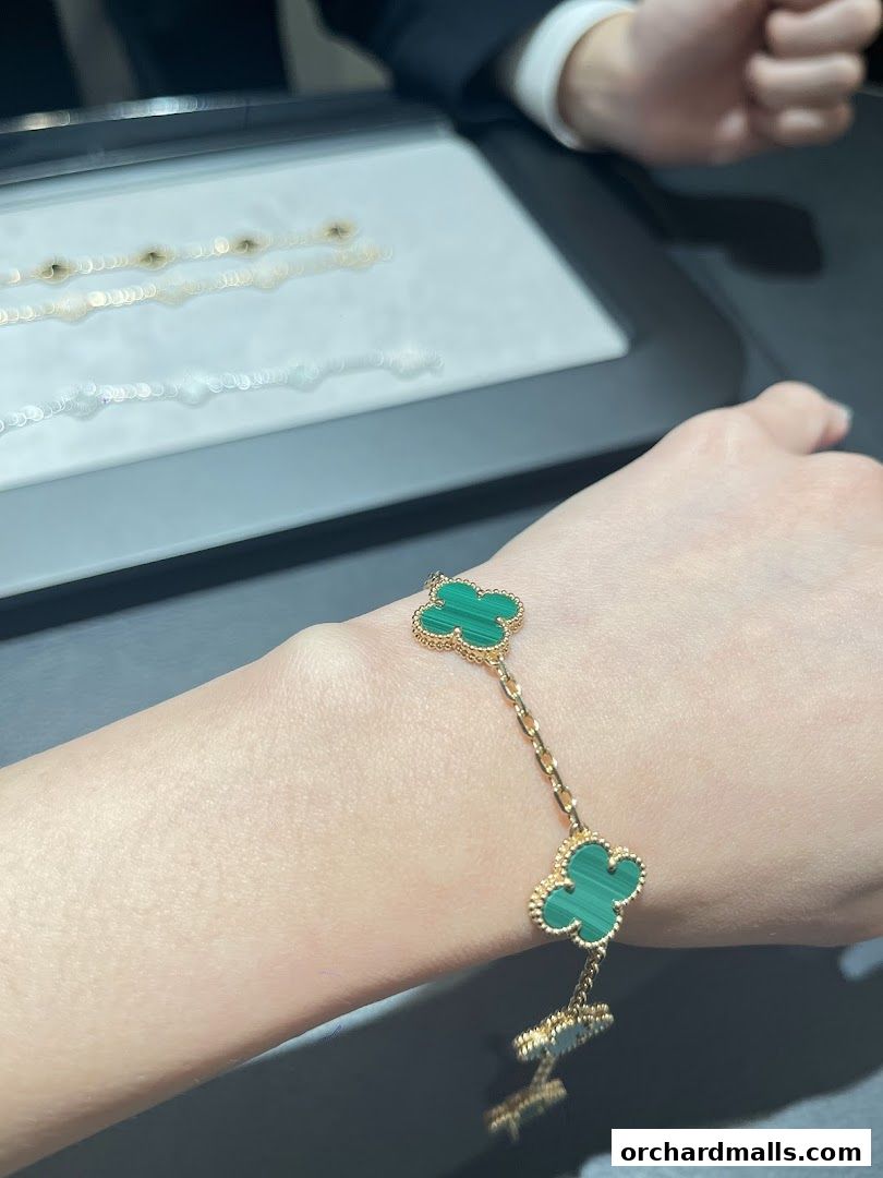 A hand wearing a Van Cleef & Arpels Alhambra bracelet with malachite clover motifs.