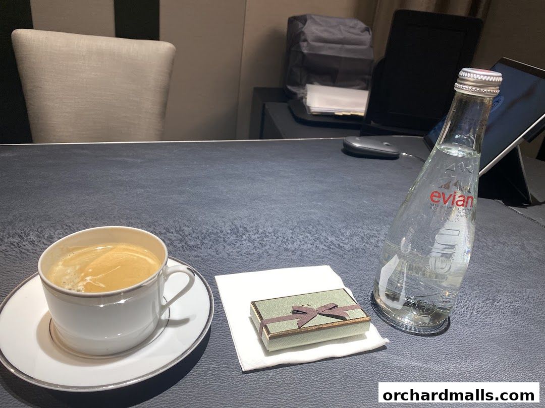 A cup of coffee, a small gift box, and a bottle of Evian water on a dark surface.
