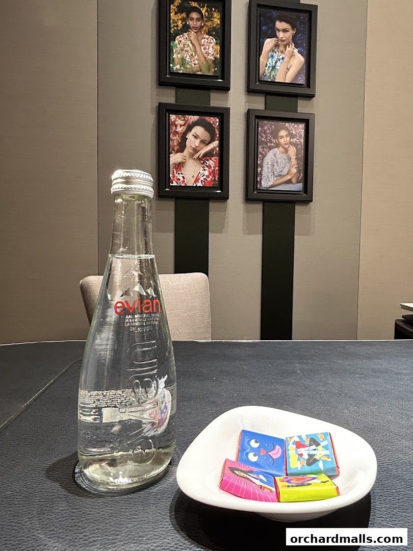 A bottle of Evian water and a dish of chocolates are on a table with framed fashion portraits on the wall.