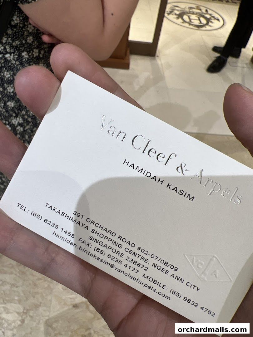 A business card for Van Cleef & Arpels, Singapore, held by a person.