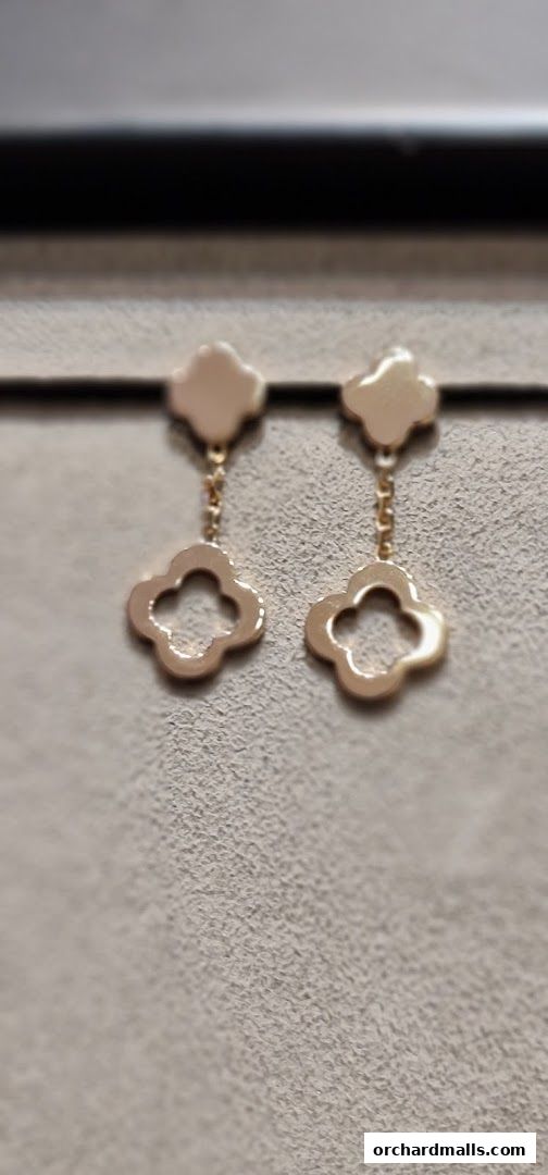 A pair of elegant gold clover-shaped dangling earrings displayed on a textured surface.