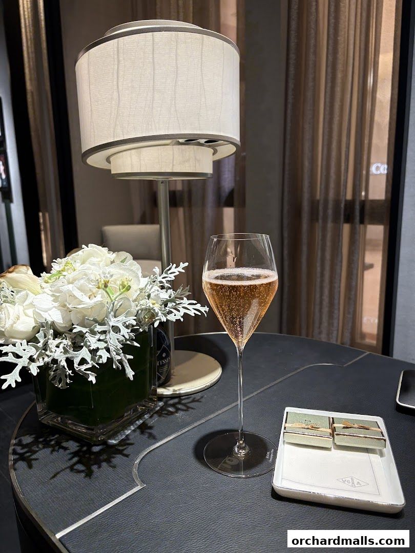 A glass of champagne and chocolates on a table with flowers and a lamp.