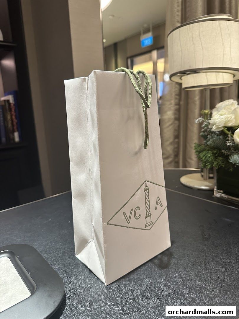 A white shopping bag with the Van Cleef & Arpels logo sits on a dark surface.
