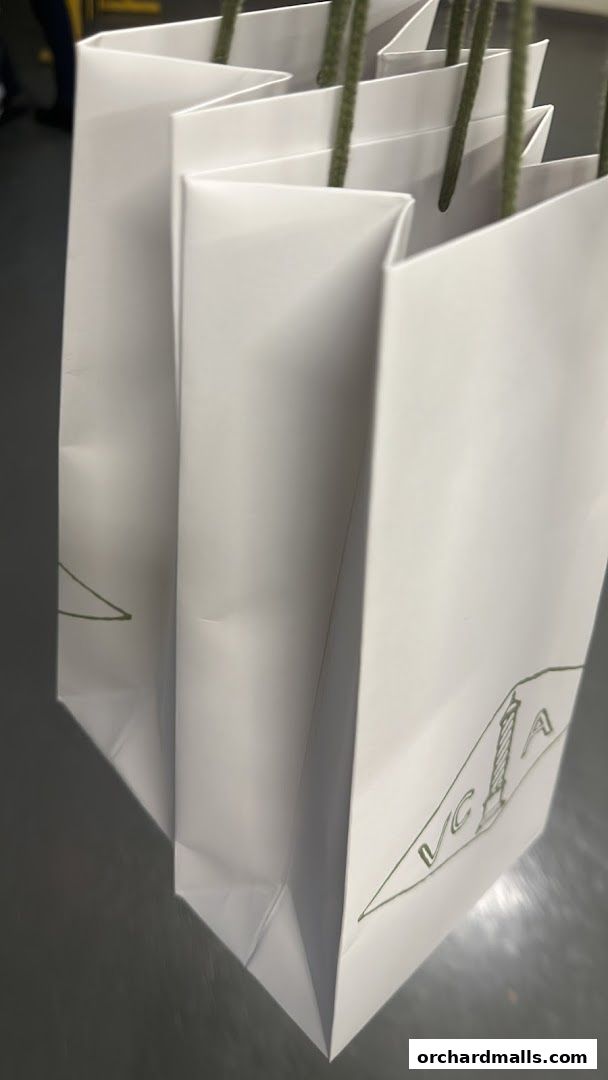 Several white shopping bags with green handles and a logo are lined up.