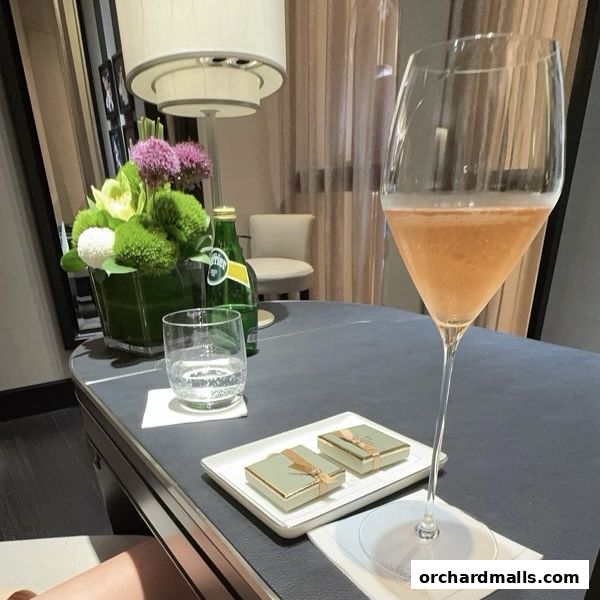A table setting with a glass of rosé, Perrier, and two small gift boxes.