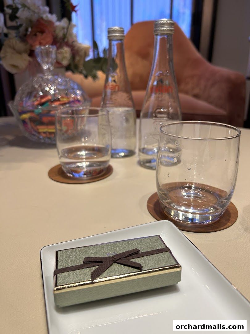 A small gift box with a ribbon sits on a tray with glasses and Evian water bottles.