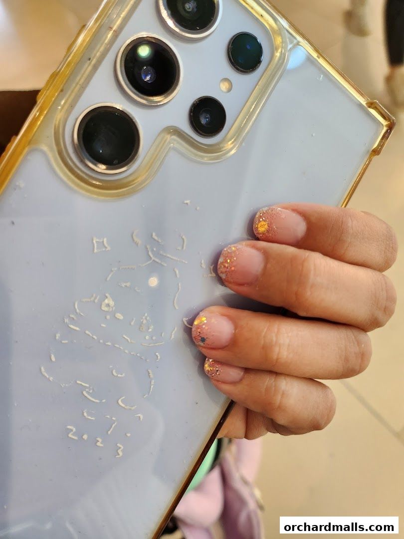 A hand with glittery nails holds a phone with a light purple case and camera array.