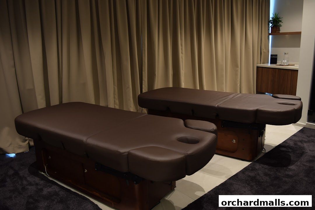 Two massage beds are set up in a spa room with beige curtains in the background.