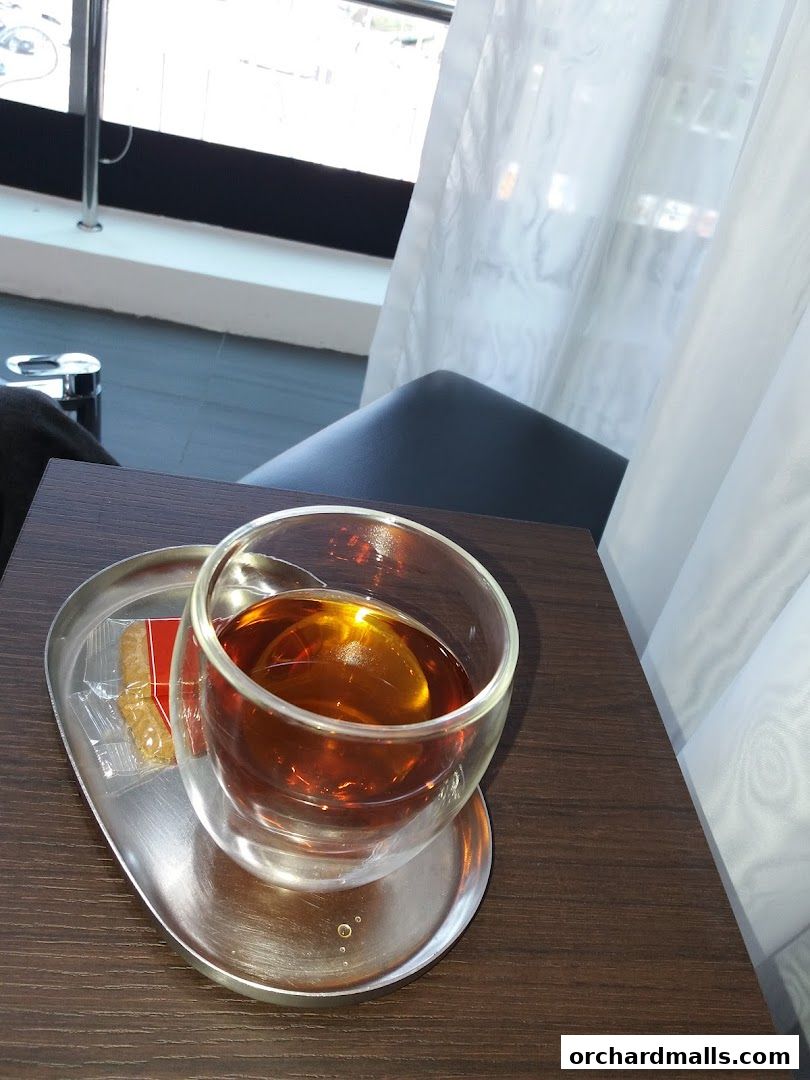 A glass of amber tea with a biscuit on a silver tray, served on a wooden table.