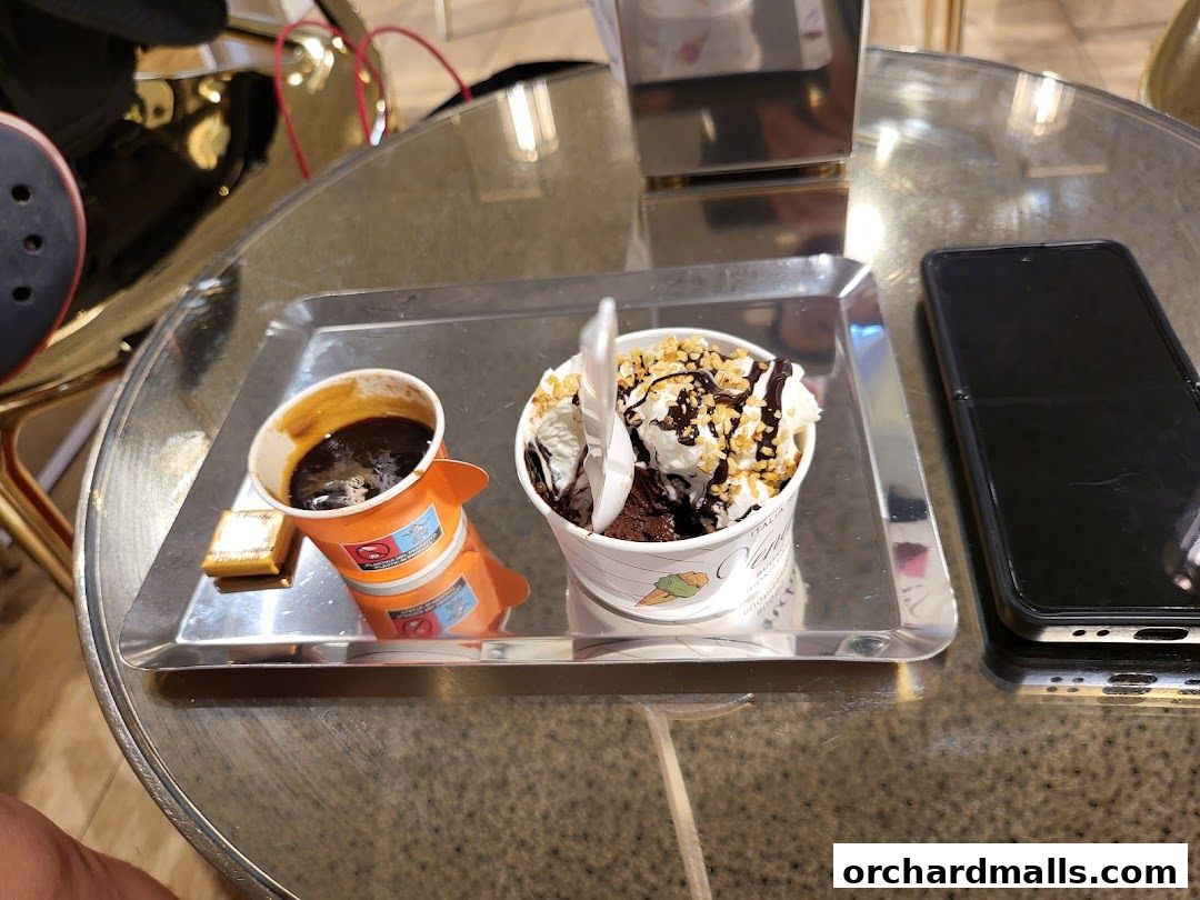 A cup of coffee and a dessert with ice cream and chocolate on a tray next to a phone.