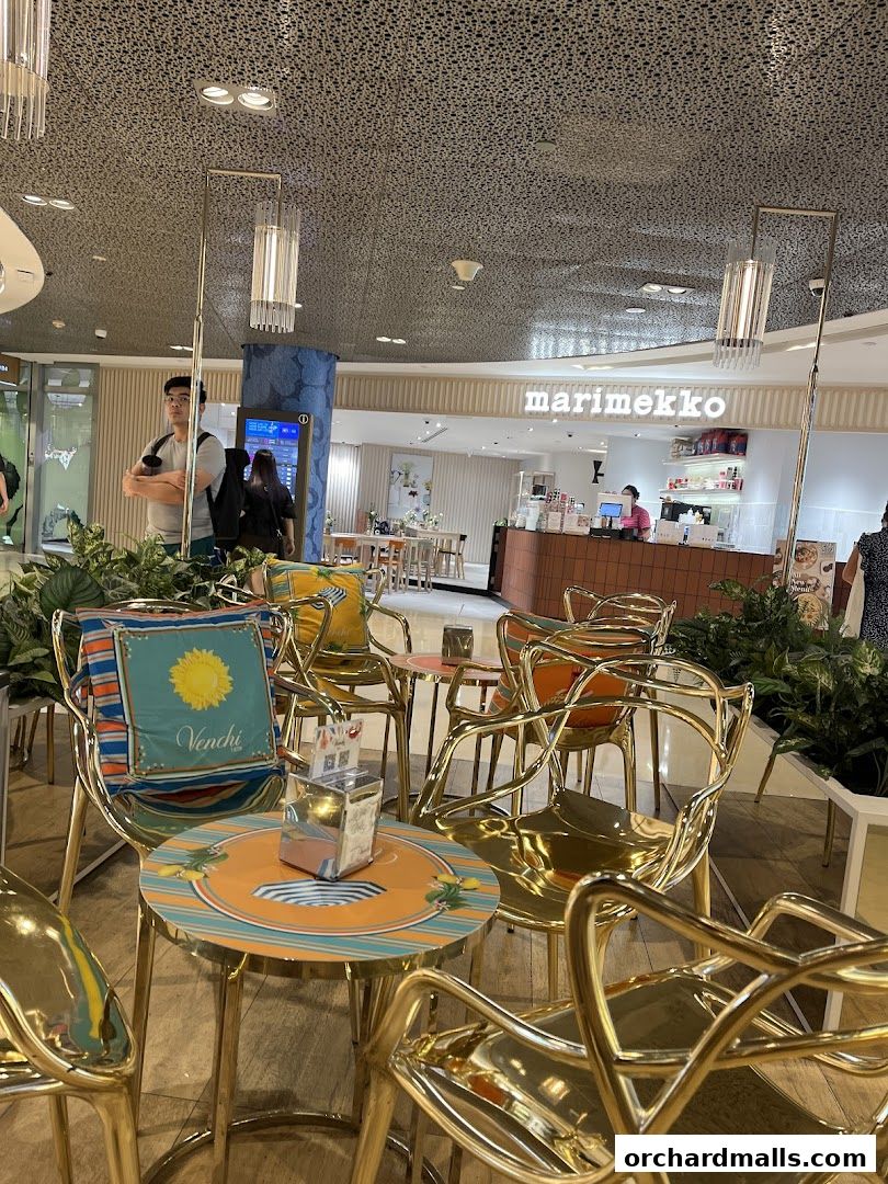 Interior seating area with stylish gold chairs and tables, featuring a Marimekko store in the background.
