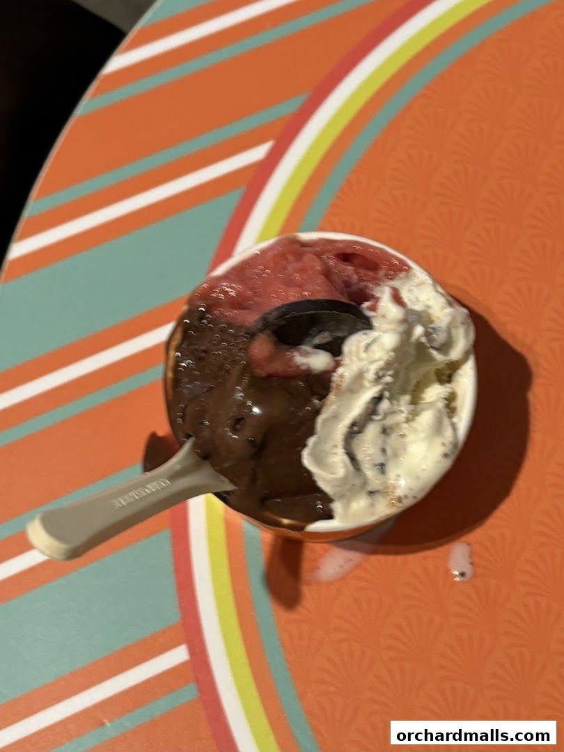 A cup of three-flavor gelato with a spoon on a colorful striped surface.