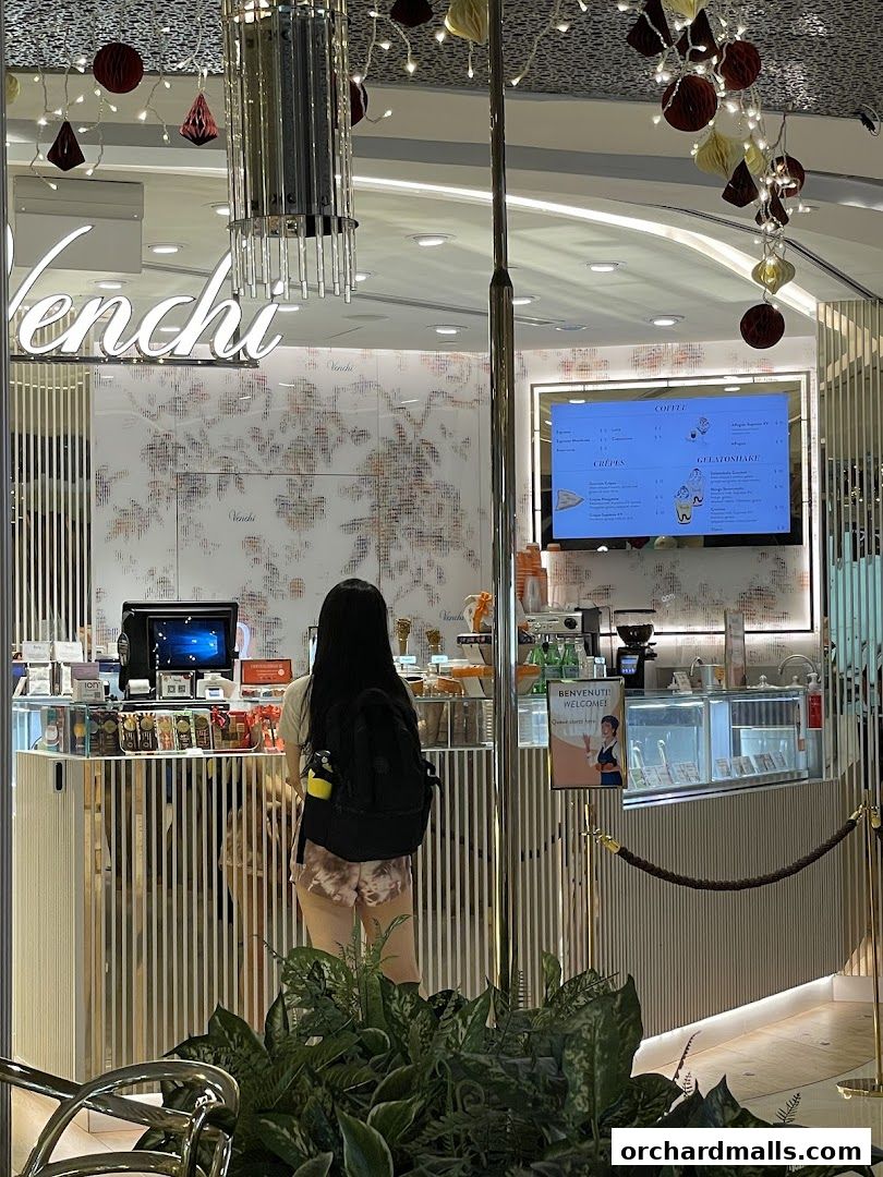 A customer stands at the counter of a Venchi store, with a digital menu displaying coffee and gelato options.