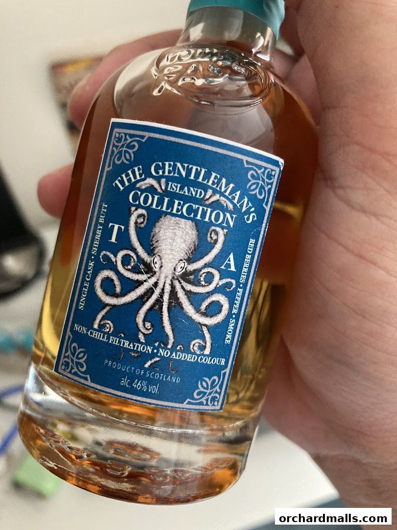 A hand holds a small bottle of "The Gentleman's Island Collection" whisky.