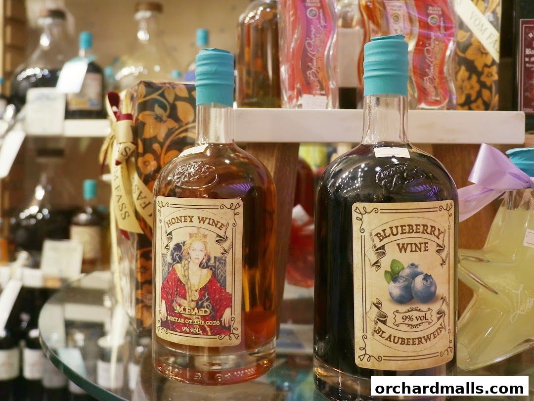 Two bottles of wine, one honey wine and one blueberry wine, are displayed on a shelf.