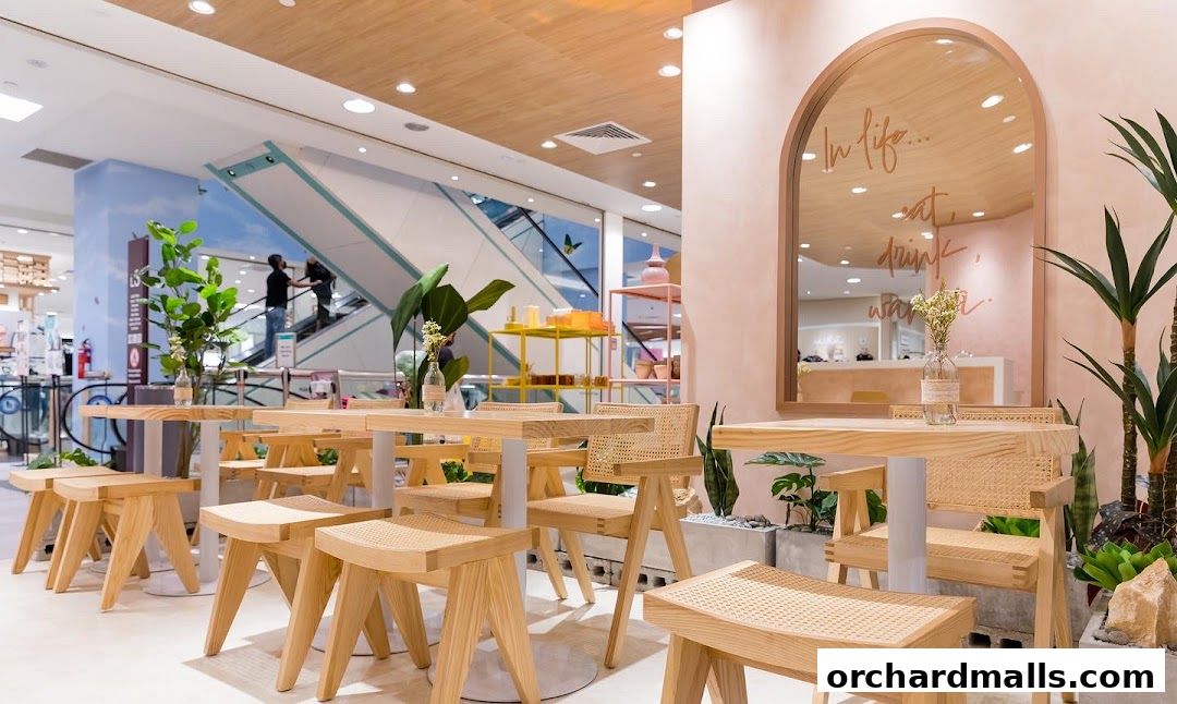 Interior of a cafe with wooden tables, chairs, and plants, featuring a mirror with text.