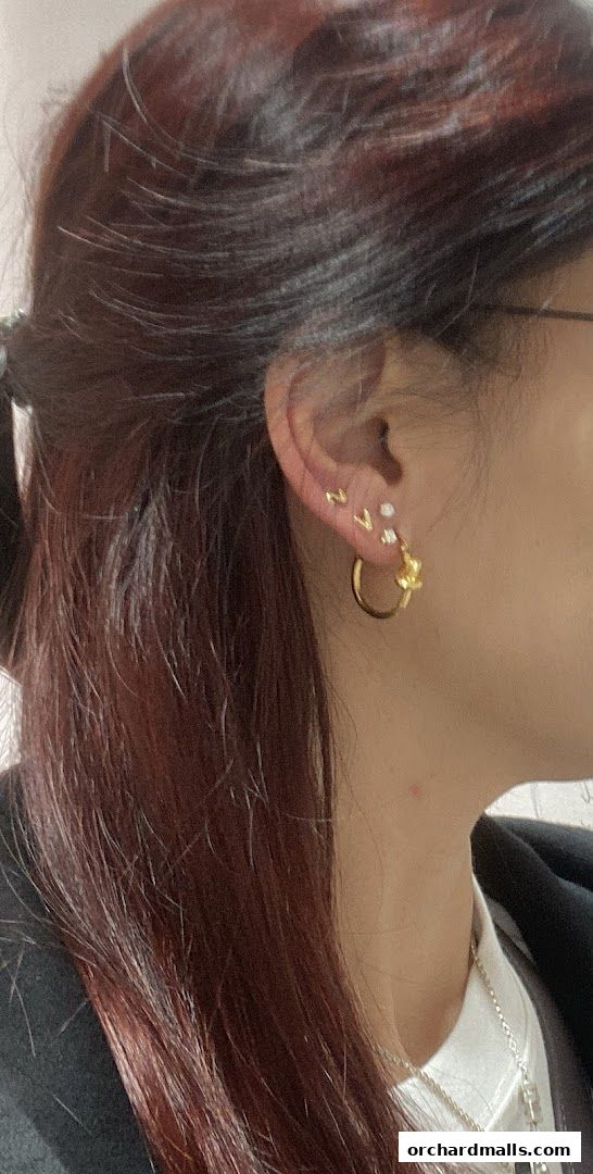 Close-up of a woman's ear adorned with delicate gold jewelry, including studs and a hoop.