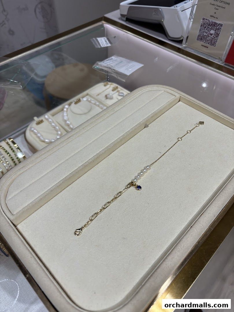 A delicate gold bracelet with pearls and a sapphire charm displayed in a jewelry store.