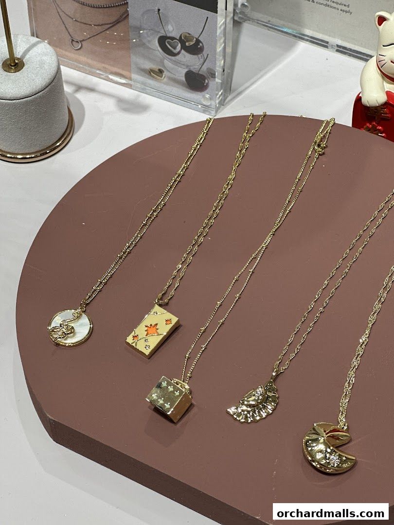 A display of unique gold necklaces with various charms on a brown stand.
