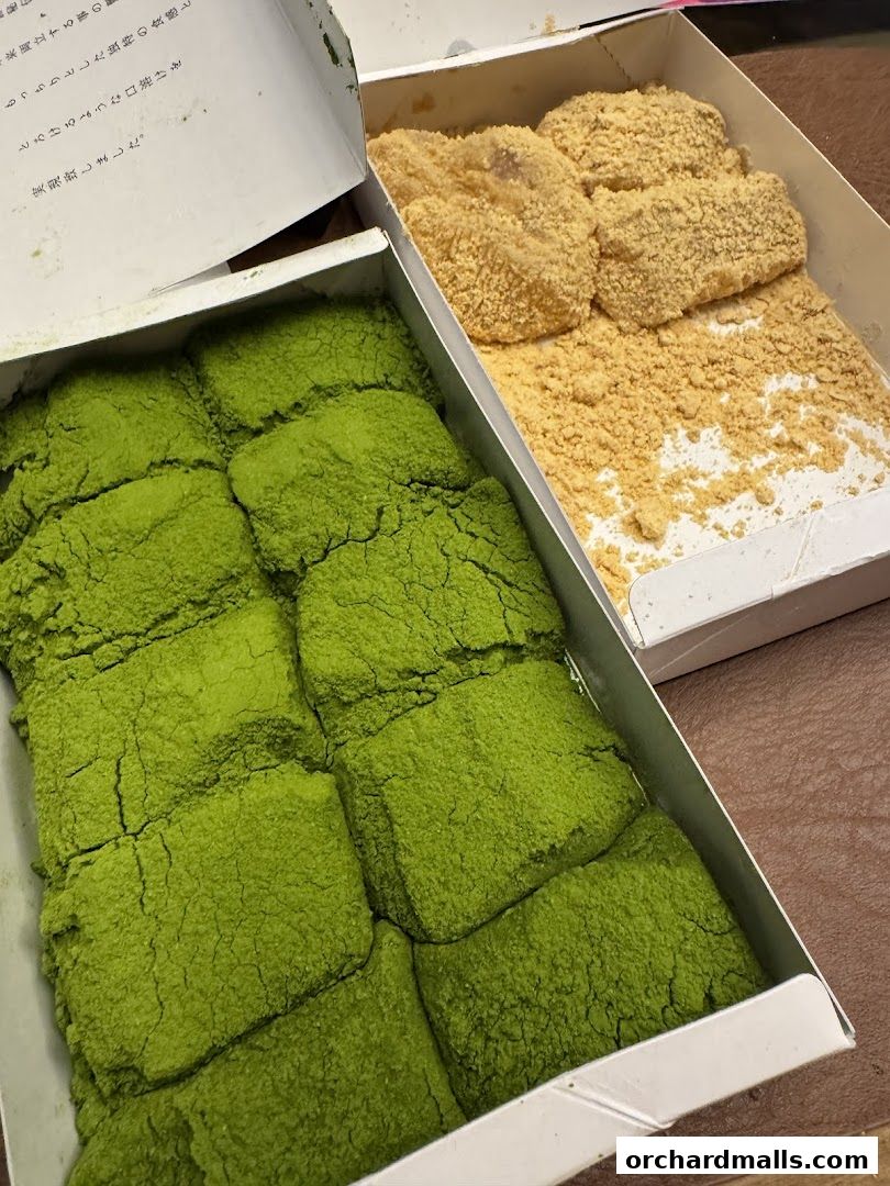 Two boxes of warabimochi, one covered in matcha powder, the other in kinako powder.