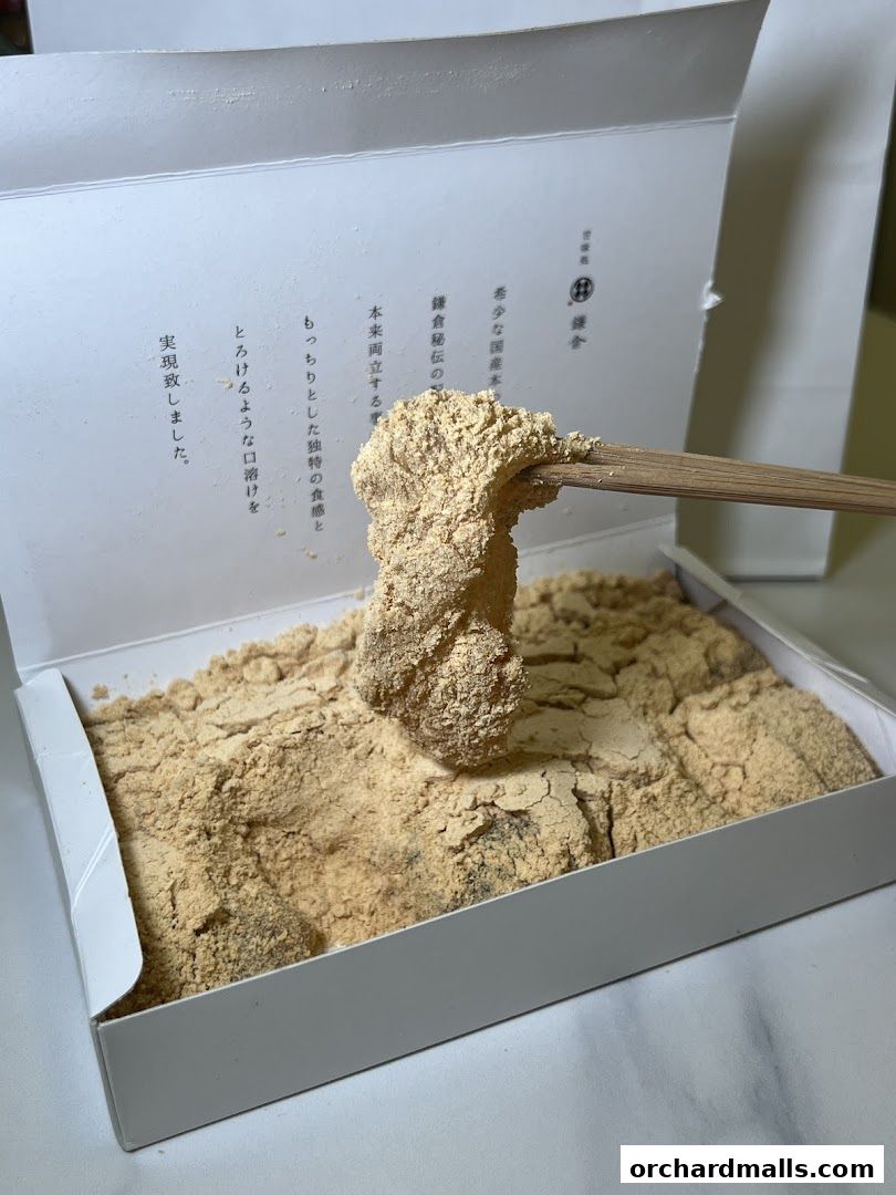 A box of Warabimochi dusted with kinako powder, with chopsticks lifting a piece.
