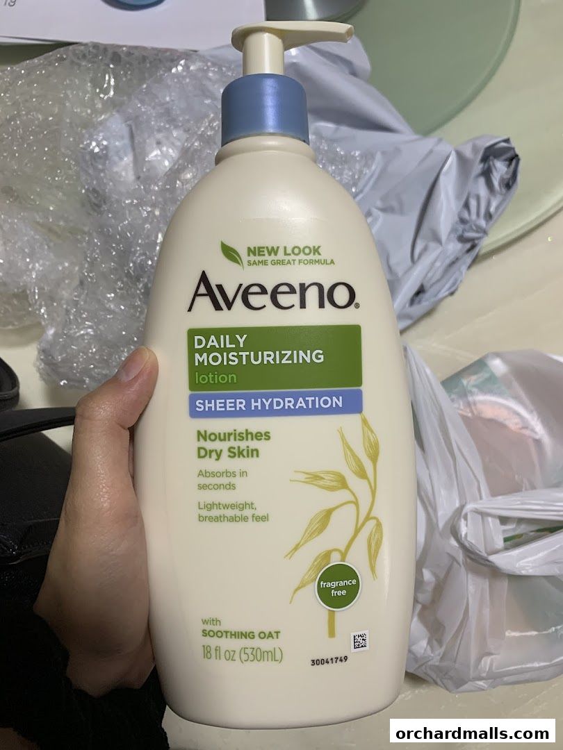 A hand holds a bottle of Aveeno Daily Moisturizing Lotion with Sheer Hydration.
