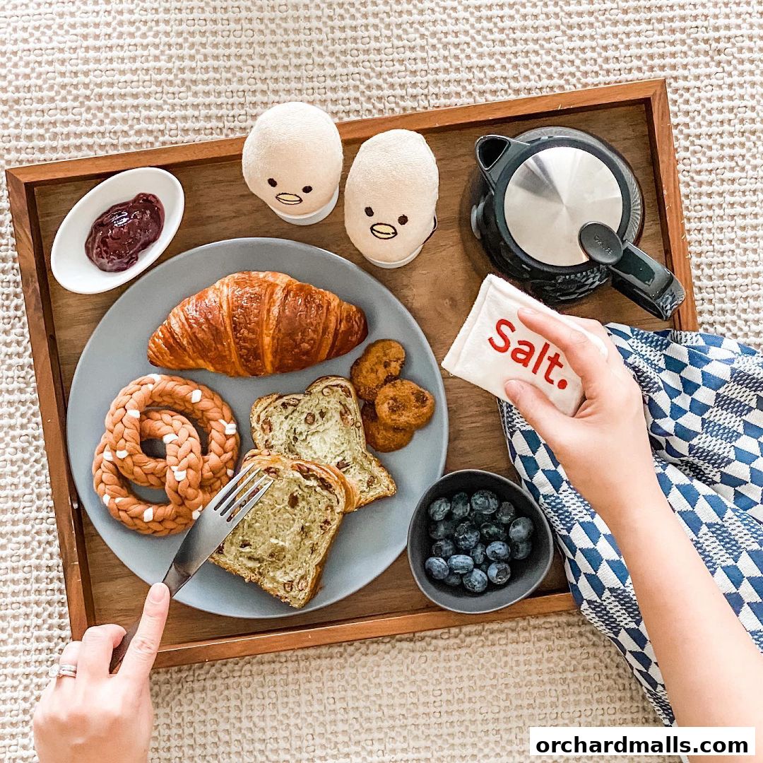 A person is about to eat a breakfast tray with a croissant, bread, and jam.