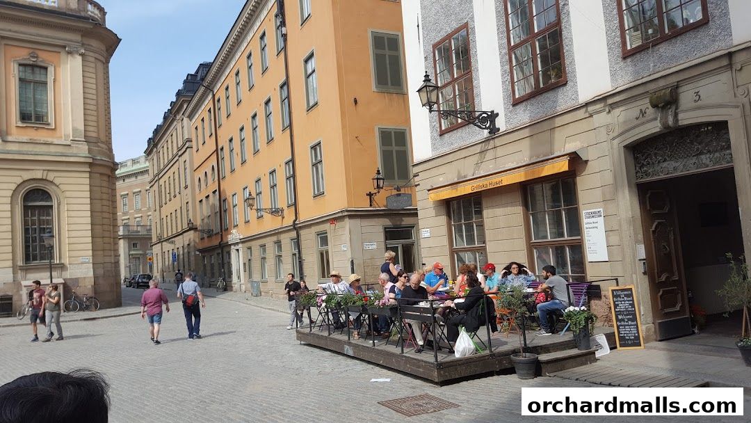 People dining at outdoor tables in front of a building with a yellow awning.