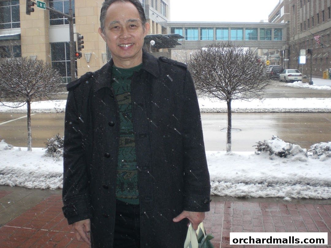 A man in a coat stands outside in the snow, holding a bag.