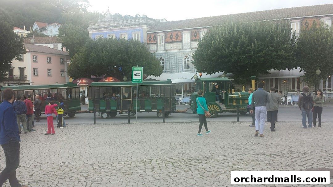 A green tourist train is parked on a cobblestone street with people around.