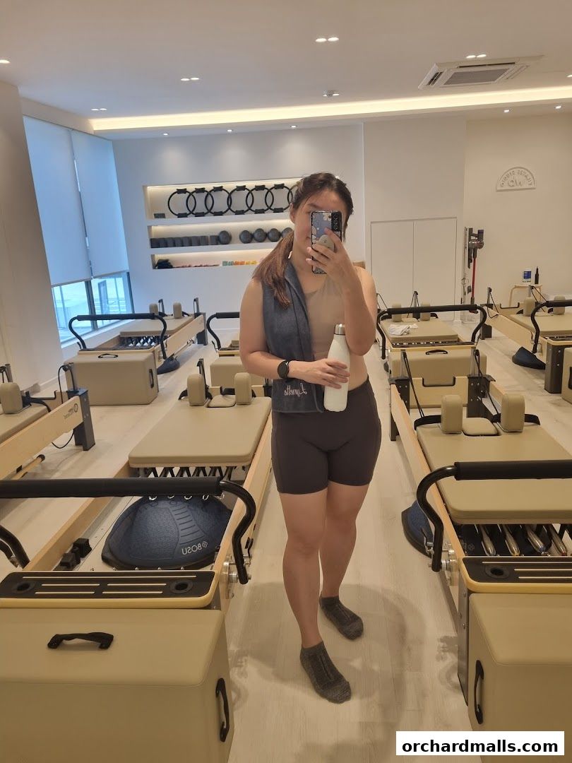 A woman takes a selfie in a bright Pilates studio with reformers and equipment.