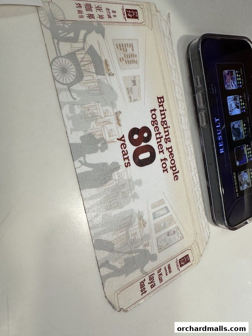 A Ya Kun Kaya Toast promotional flyer celebrating 80 years, next to a smartphone.