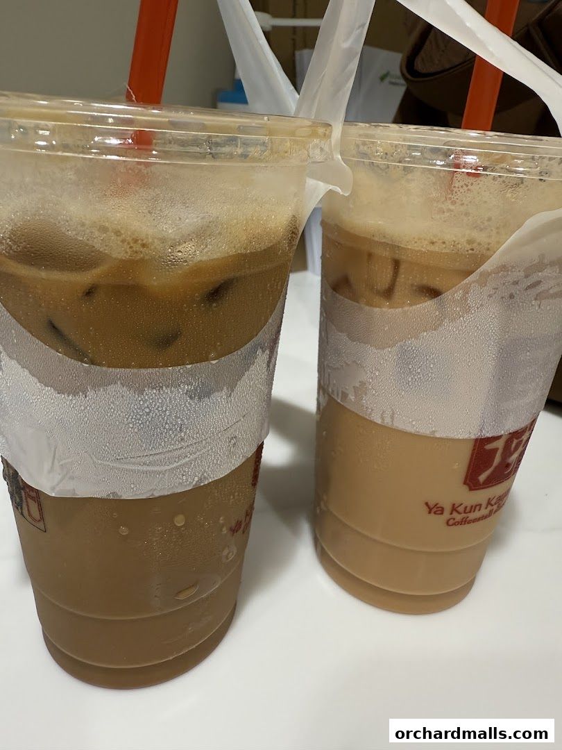 Two iced coffee drinks with straws in plastic cups, branded with Ya Kun Kaya Toast.