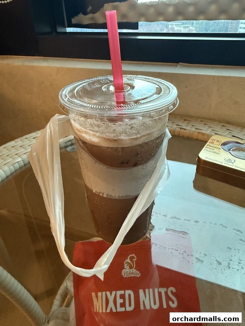 A close-up of an iced beverage with a pink straw, next to a packet of mixed nuts.